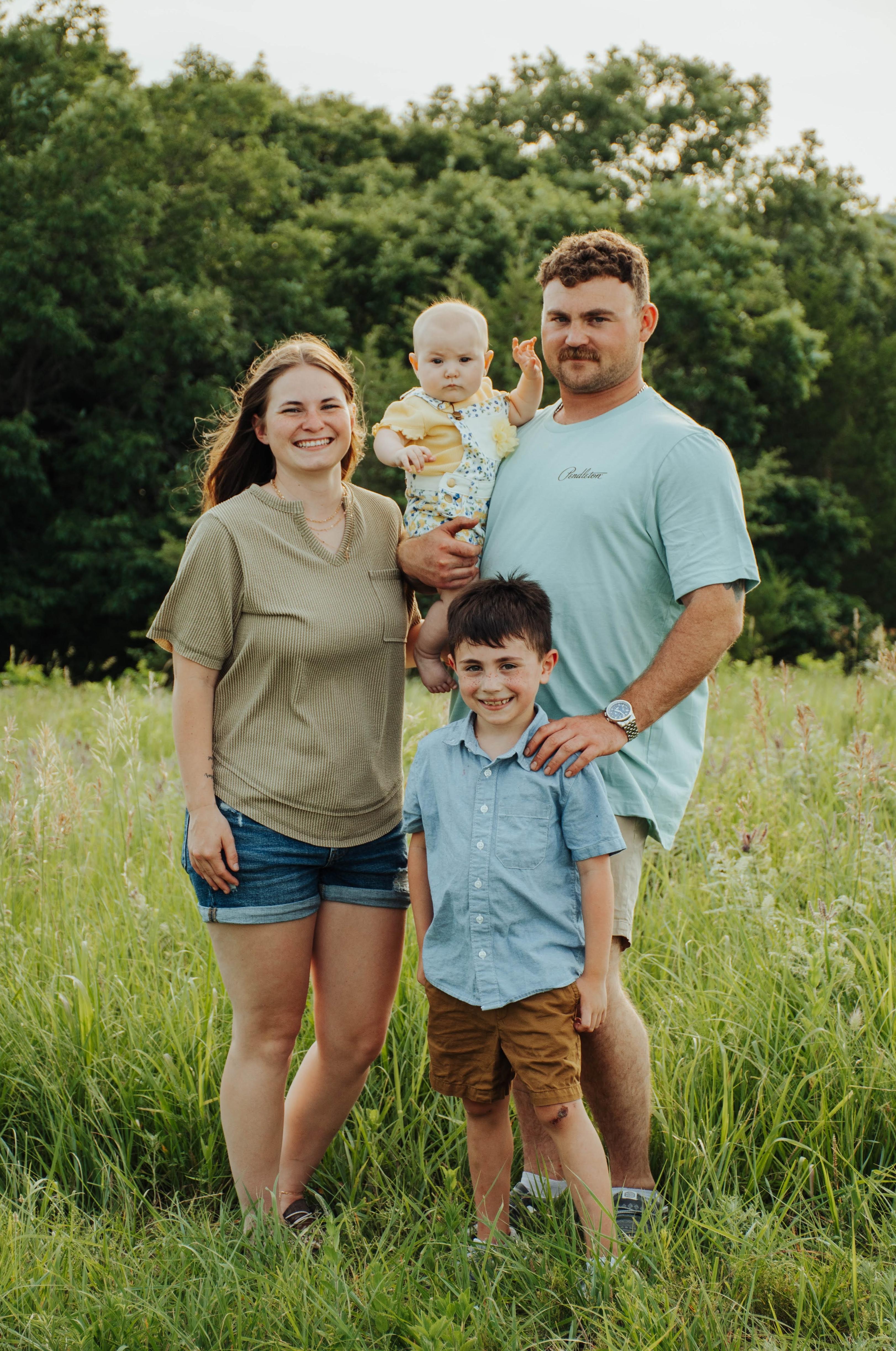 family standing in a field with trees in background