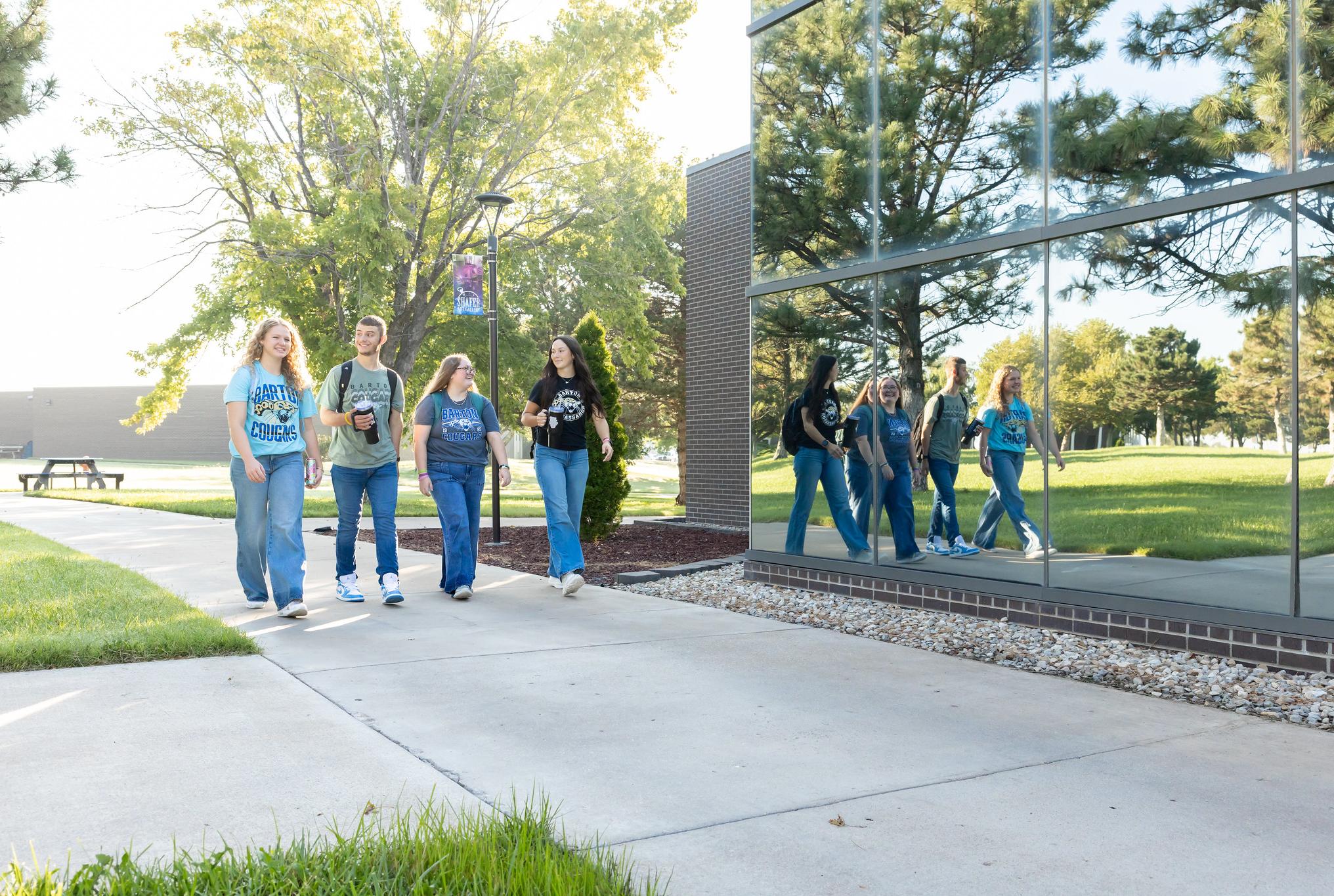 students walking on a college campus in front of a building with a lot of windows
