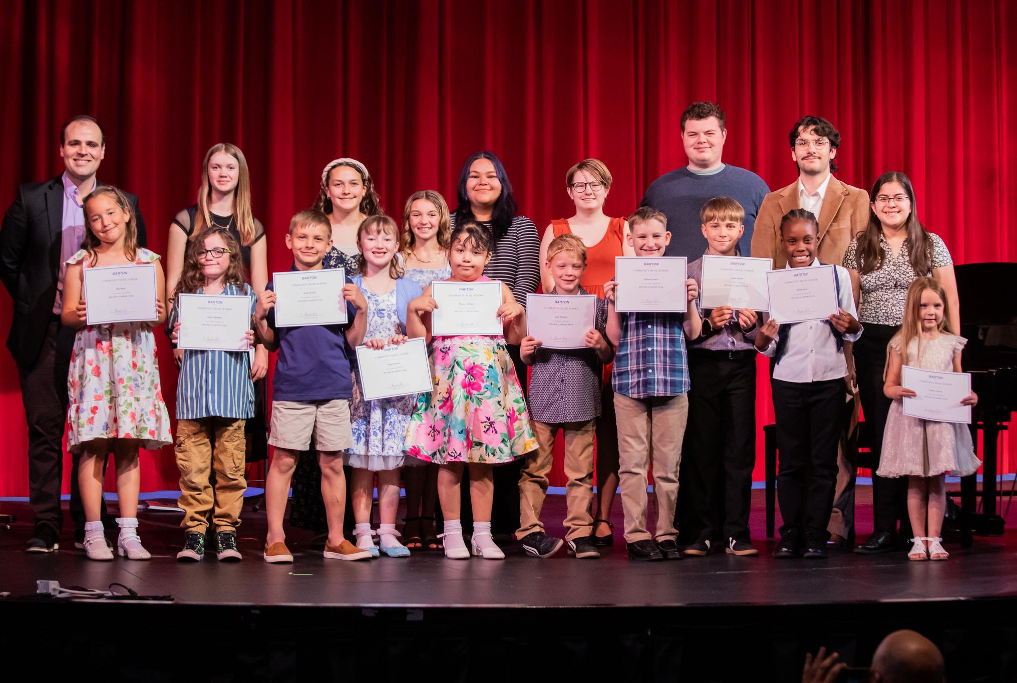 kids standing on stage with certificates and their music teachers